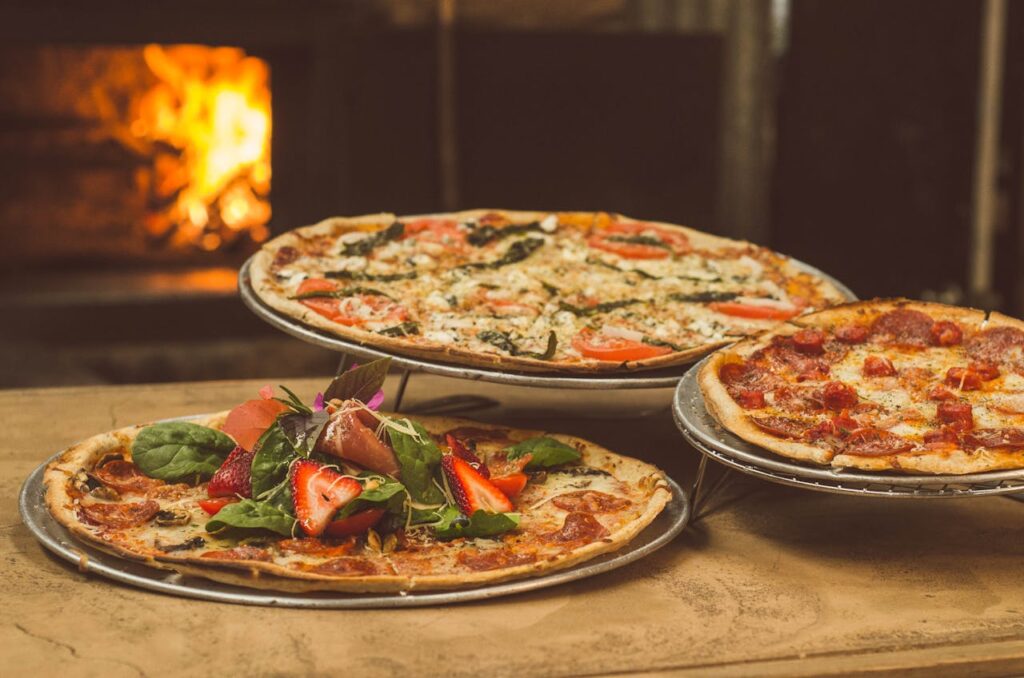 pexels-photo-1566837 Trio of gourmet pizzas with unique toppings near a wood-fired oven, ideal for food enthusiasts.